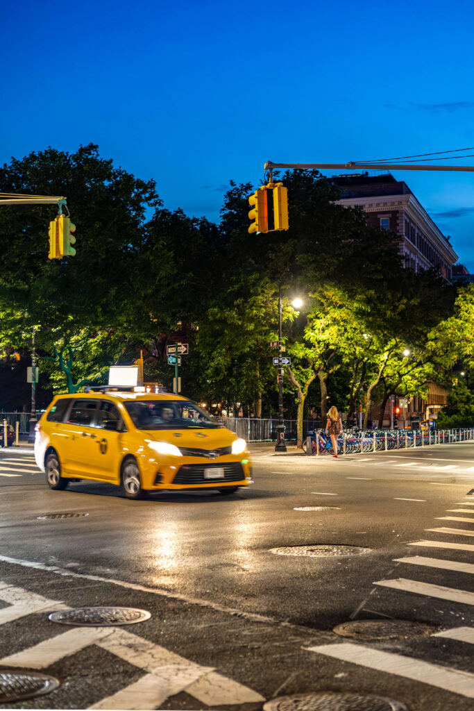 Yellow taxi illuminated by streetlights at dusk.