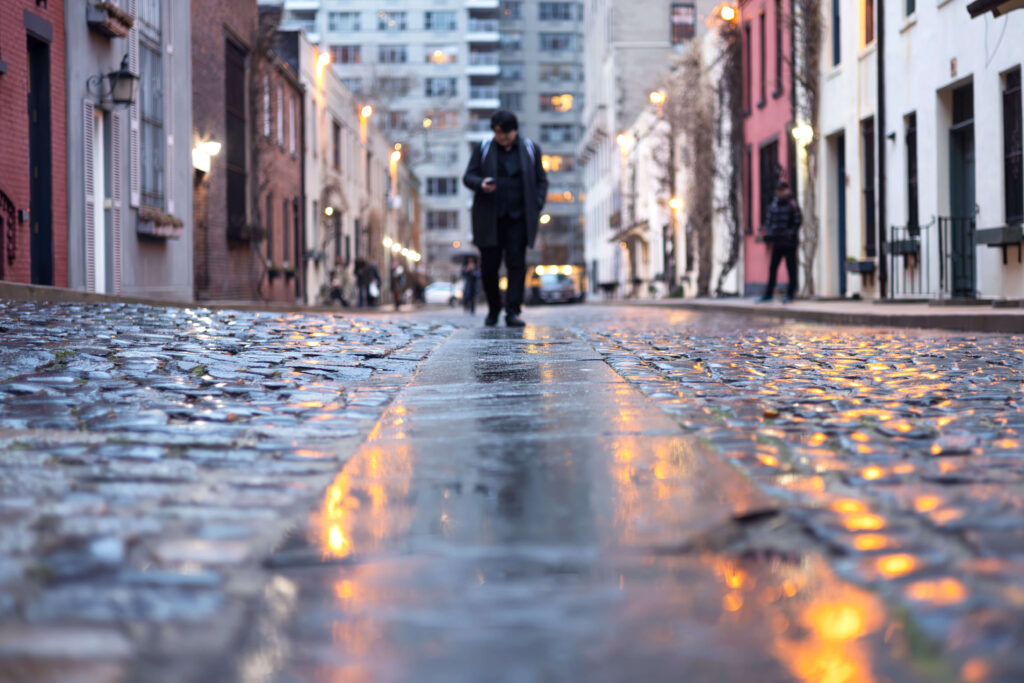 Cobblestone street of Washington Mews lit by street lights at twilight.